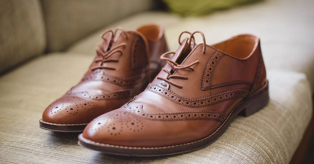 Par de zapatos oxford brogue marrones colocados de manera elegante en un sofá moderno.